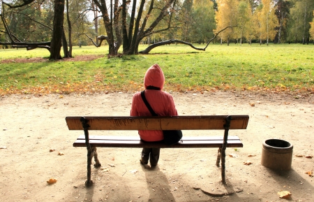 Lonely woman sitting on the bench in autumnal park.の写真素材