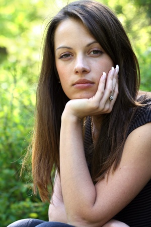 Woman with long brunette hair on natural green background. She rest her chin on her hand.の写真素材