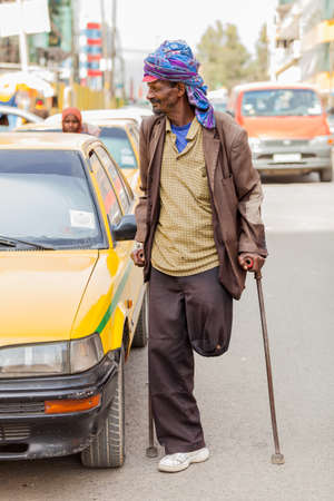 Addis Ababa, Ethiopia, January 27, 2014, Old Arabic man using crutches next to a yellow taxi in...