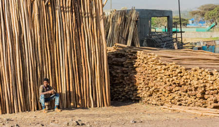 Addis Ababa, Ethiopia, January 30, 2014, African man sitting next to a stack of wooden scaffolding on the side of a roadのeditorial素材