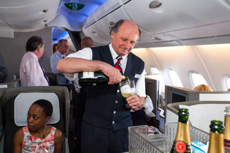 Johannesburg, South Africa - February 06, 2014: Male cabin crew pouring a glass of Champaign in...