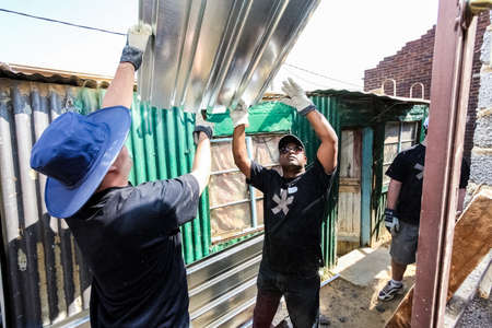 Soweto, South Africa - September 05, 2009: Diverse Community Outreach program helping to install metal roofing on a small affordable house in local townshipのeditorial素材