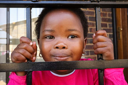 Soweto, South Africa - September 11, 2009: Little African Girl holding onto security bars in a Soweto Township homeのeditorial素材