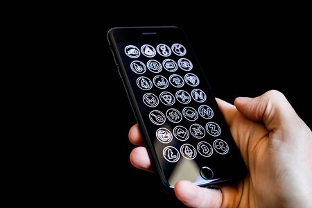 Caucasian Male Hand Holding a Mobile Phone with Cryptocurrency Altcoin Icons on the screen