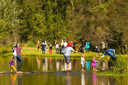 Johannesburg, South Africa, 05/10/2014, Family crossing a stream on stepping stones at The Winter Sculpture Fair at Nirox Sculpture Parkのeditorial素材