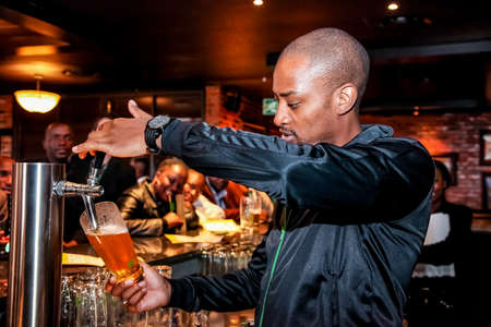 Johannesburg, South Africa - April 24, 2012: African Barman pouring a pint draft beer at barman...