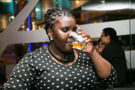 Johannesburg, South Africa - December 10 2014: Young African Woman drinking Whiskey out of a tumbler...