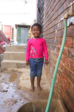 Soweto, South Africa - September 11, 2009: Little African Girl getting splashed by hosepipe water in a Soweto Township back yardのeditorial素材