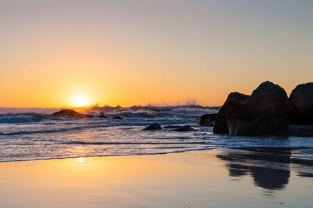Photographed on a West coast facing beach in Cape Town South Africa. Rough waves at sunset on a sandy beach with reflections on the waterの写真素材