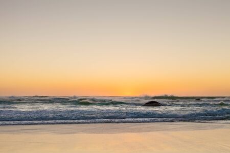 Photographed on a West coast facing beach in Cape Town South Africa. Rough waves at sunset on a sandy beach with reflections on the waterの写真素材