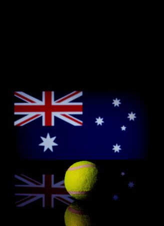Yellow Tennis Ball on black mirror with Australian Flag in the background out of focusの写真素材
