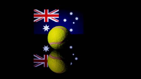 Yellow Tennis Ball on black mirror with Australian Flag in the background out of focusの写真素材