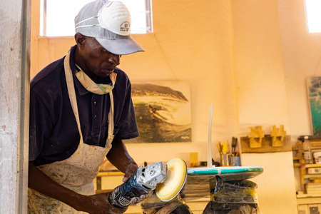 Cape Town, South Africa - March 23, 2021: An African Craftsman surfboard Shaper working in a repair...
