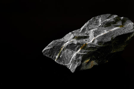 Macro Close up image of raw material Manganese Ore rock isolated on black reflective background
