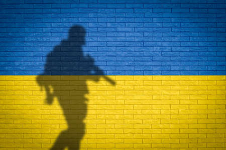Conceptual image of war between Russia and Ukraine with shadow of soldier against wall with national flag backgroundの写真素材