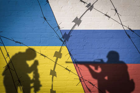 Conceptual image of war between Russia and Ukraine with shadow of soldier against wall with national flag backgroundの写真素材
