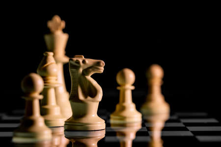 Close up of Chess pieces on a reflective mirror board surface with a plain black backgroundの写真素材