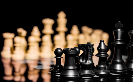 Close up of Chess pieces on a reflective mirror board surface with a plain black backgroundの写真素材
