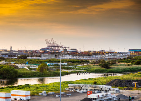Cape Town, South Africa - October 12, 2022: Harbour cranes and shipping containers behind river