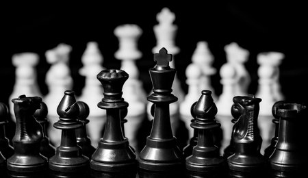 Close up of Chess pieces on a reflective mirror board surface with a plain black backgroundの写真素材