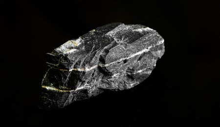 Macro Close up image of raw material Manganese Ore rock isolated on black reflective background