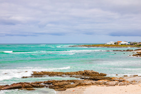 Tranquil coastline landscape with azure sky, sand, rocks, and gentle waves, South Africa