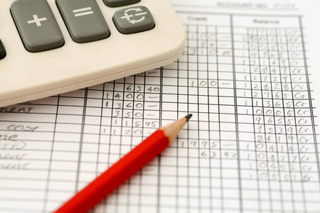 Handwritten Accounting ledger showing bookkeeping using pencil and calculator.の写真素材