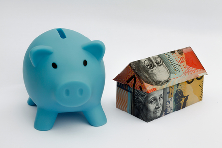 Origami money house next to a blue piggy bankの写真素材