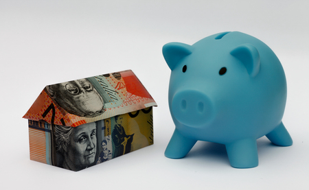 Origami money house next to a blue piggy bankの写真素材