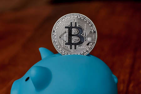 Large Bitcoin being deposited into a piggy bankの写真素材