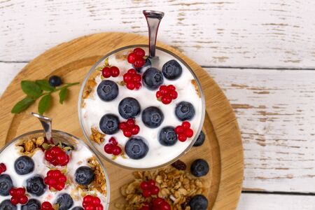 Two ice-cream bowls with a dessert. Yogurt, muesli and  fresh berries of blueberry, bog bilberry ...