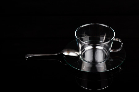 Glass cup on a saucer with a spoon on a black tableの写真素材