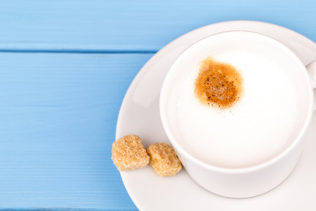 Cup of cappuccino and with cane sugar on a blue tableの写真素材