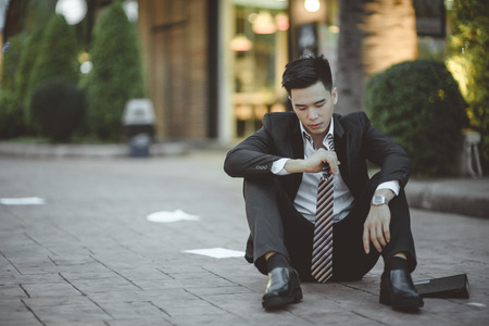 Tired or stressed businessman sitting on the walkway in the city after his work. Image of Stressed businessman concept, young caucasian businessman tired from work sitting at stairs, unemployment.の写真素材