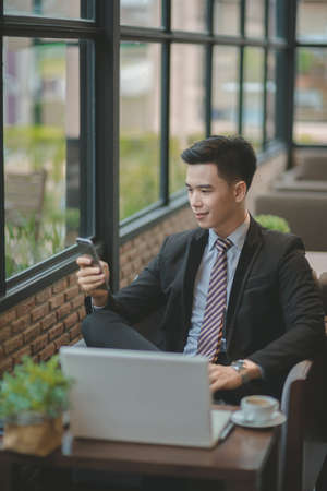 Happy  businessman using cellphone while sitting on sofa at his modern home.Concept of young people working on mobile devices.Blurred backgroundの写真素材