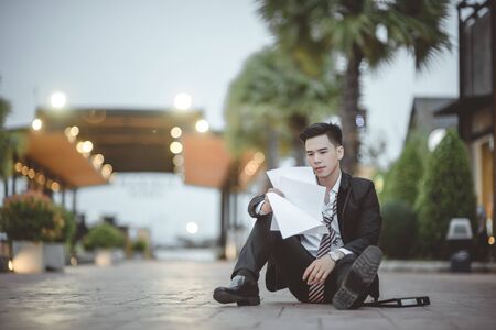 Tired or stressed businessman sitting on the walkway in the city after his work. Image of Stressed businessman concept, young caucasian businessman tired from work sitting at stairs, unemployment.の写真素材