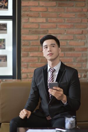 Happy  businessman using cellphone while sitting on sofa at his modern home.Concept of young people working on mobile devices.Blurred backgroundの写真素材