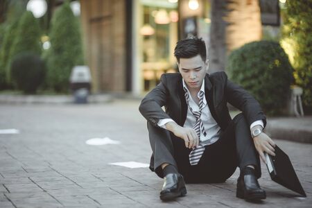 Tired or stressed businessman sitting on the walkway in the city after his work. Image of Stressed businessman concept, young caucasian businessman tired from work sitting at stairs, unemployment.の写真素材