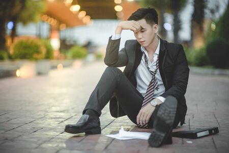 Tired or stressed businessman sitting on the walkway in the city after his work. Image of Stressed businessman concept, young caucasian businessman tired from work sitting at stairs, unemployment.の写真素材