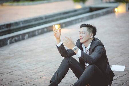 Tired or stressed businessman sitting on the walkway in the city after his work. Image of Stressed businessman concept, young caucasian businessman tired from work sitting at stairs, unemployment.の写真素材