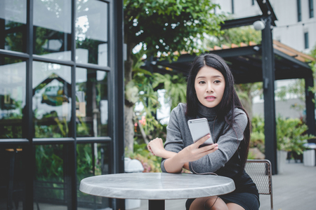 Portrait of young businesswoman use mobile phone while sitting in comfortable coffee shop during work break, charming happy female reading fashion news on cell telephoneの写真素材