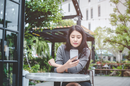 Portrait of young businesswoman use mobile phone while sitting in comfortable coffee shop during work break, charming happy female reading fashion news on cell telephoneの写真素材