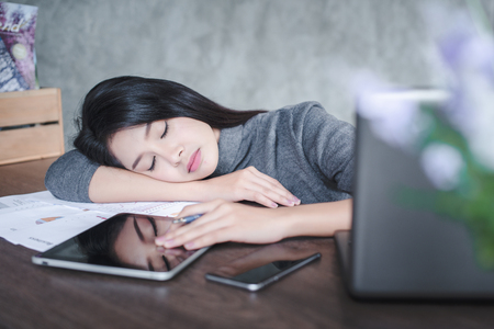 Young attractive Asian business woman sleeping, drowsing or taking a nap at her desk, Tired business woman accountant with bills and paper folders in office, tired young business woman with laptop.の写真素材