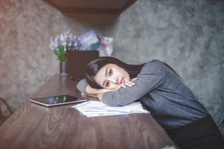 Young attractive Asian business woman sleeping, drowsing or taking a nap at her desk, Tired business woman accountant with bills and paper folders in office, tired young business woman with laptop.の写真素材