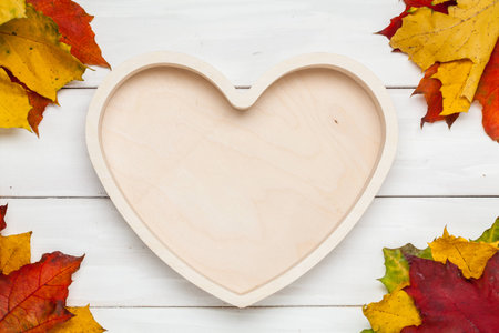 Wooden heart on color leaf background. Empty container for montage product with copy space. Autumn time.の写真素材
