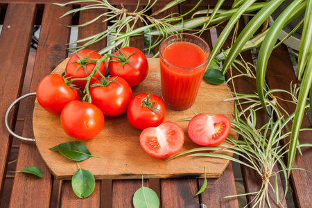 Red tomato and juice in glass fruit on wood background with green leafの写真素材