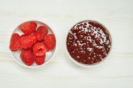 Raspberries jam with fresh red ripe on wooden background.