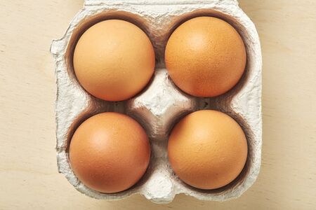 Four raw egg in packing on wooden table. Top view.