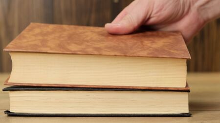 Female hand puts books on a table on wooden background. Close up.の写真素材