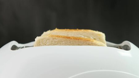 Slices of bread jump out from a white toaster. Close up.